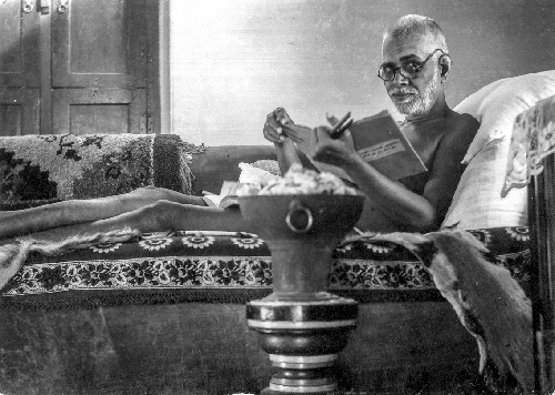 Bhagavan Sri Ramana Maharshi reclining on the couch, reading